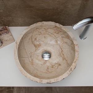 Beige marble wash basin, 40 cm in diameter, 15 cm high, with hand-carved, roughish exterior walls, for installation on a restroom countertop cabinet
