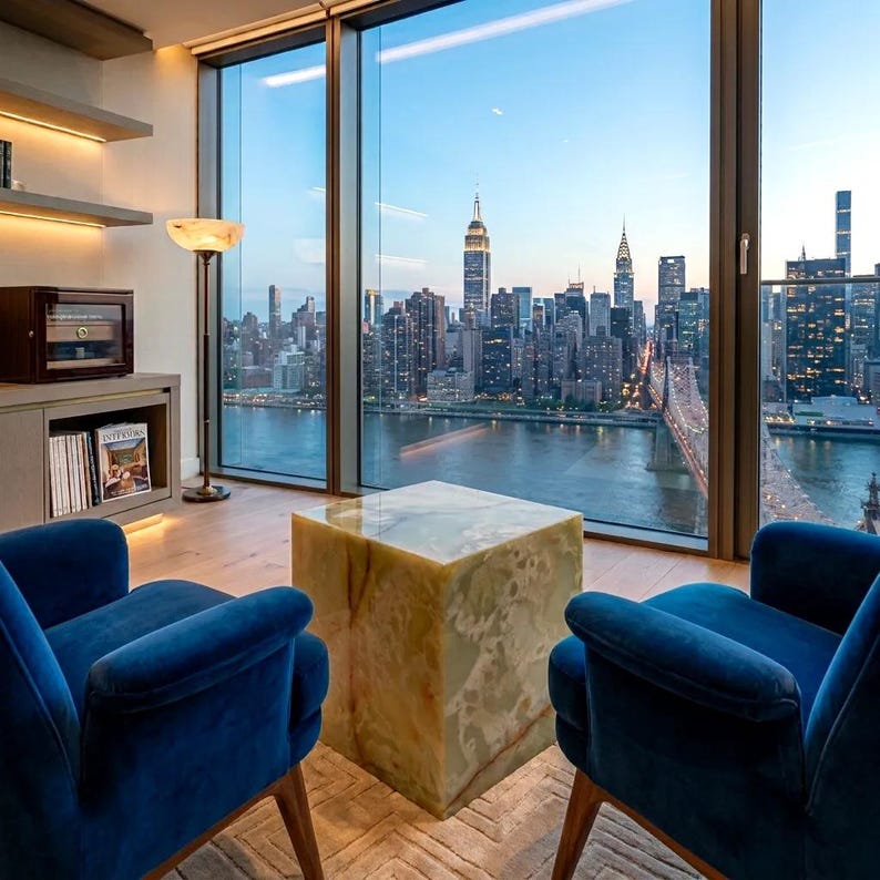 May include: Two deep blue velvet armchairs face a square, polished light green onyx side table. The furniture is positioned in a room with light wood flooring, a tall floor lamp, and a wooden cabinet, all set against a large window view of a city.
