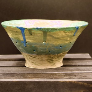 May include: A ceramic bowl with a green, blue, and brown glaze. The bowl has a wide rim and a narrow base. It has small holes in the bottom, suggesting it may be a strainer.