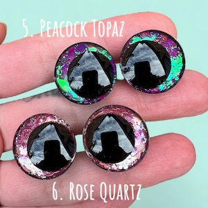 Puede incluir: Primer plano de dos pares de ojos de vidrio coloridos con pupilas negras. Los ojos est&aacute;n en una mano, y el texto "5. Peacock Topaz" y "6. Rose Quartz" es visible.