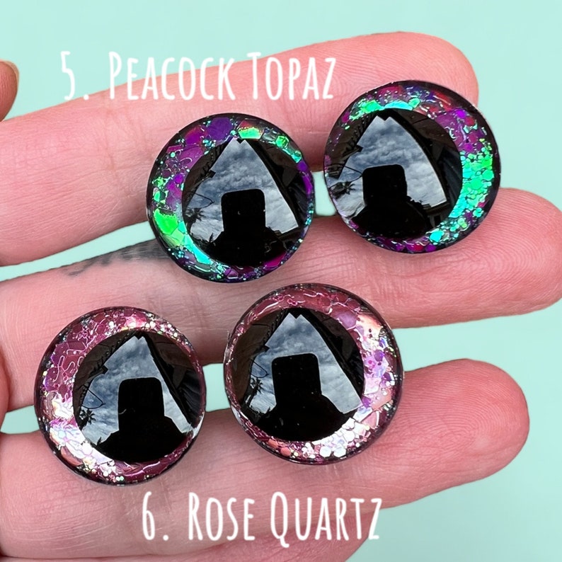 Puede incluir: Primer plano de dos pares de ojos de vidrio coloridos con pupilas negras. Los ojos est&aacute;n en una mano, y el texto "5. Peacock Topaz" y "6. Rose Quartz" es visible.