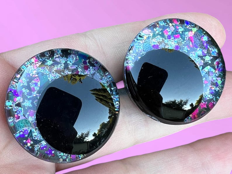 An upclose photo of a pair of hand-painted glitter safety eyes with off-set black pupils and colorful glitter with black stars and moons.