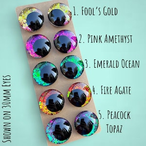 Puede incluir: Surtido de ojos de pl&aacute;stico de 30 mm con purpurina y acabados iridiscentes. Los ojos est&aacute;n dispuestos en filas sobre una superficie marr&oacute;n. Los colores incluyen: Oro de tontos, Amatista rosa, Oc&eacute;ano esmeralda, &Aacute;gata de fuego y Topacio pavo real.