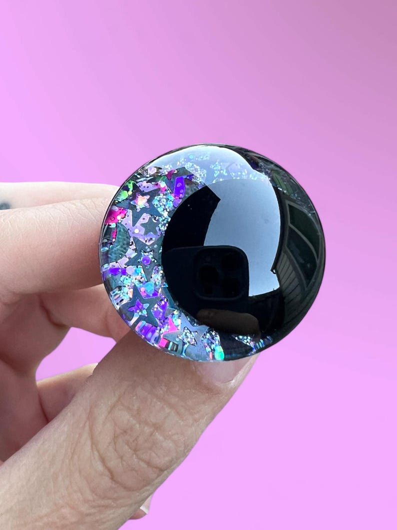 A hand painted glitter safety eye with off-set black pupils and colorful glitter with black stars and moons.