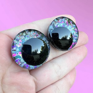 A pair of hand-painted glitter safety eyes with off-set black pupils and colorful glitter with black stars and moons.