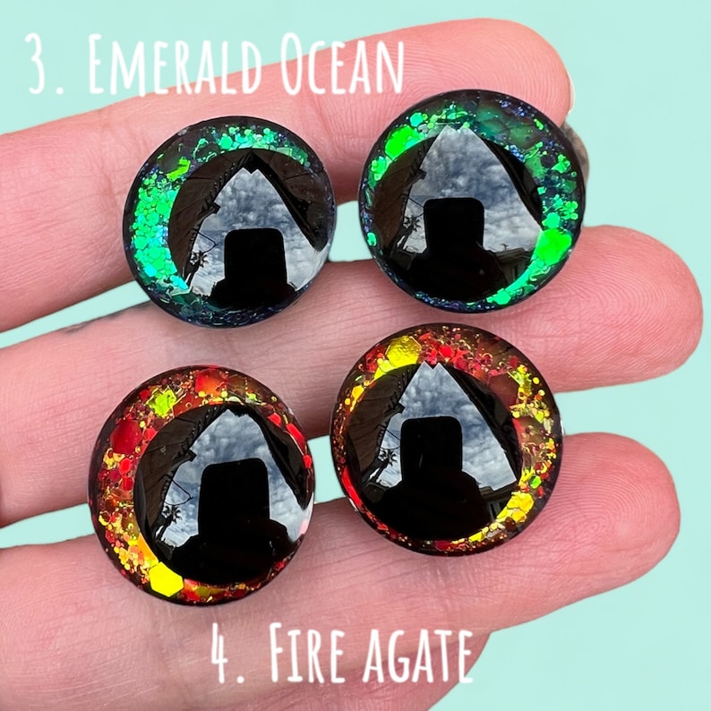 Puede incluir: Cuatro ojos redondos de resina negra con acentos de purpurina de diferentes colores. Los ojos est&aacute;n etiquetados como "3. Emerald Ocean" y "4. Fire Agate".