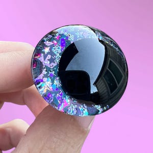 A hand painted glitter safety eye with off-set black pupils and colorful glitter with black stars and moons.