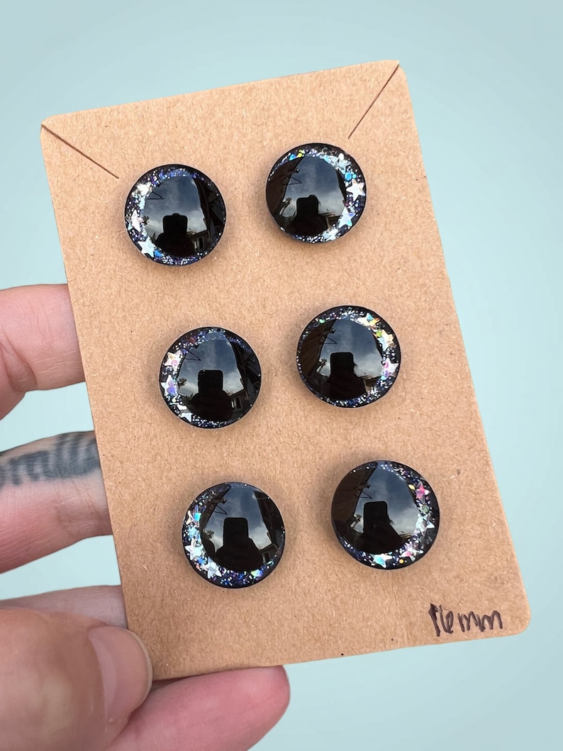 Three pairs of 16mm hand painted glittery safety eyes. They have off-set black pupils and galaxy glitter and silver stars.