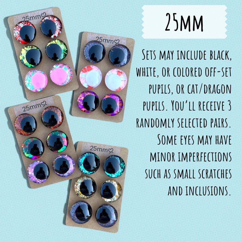 May include: Assorted 25mm craft eyes in various colors, including black, white, pink, and iridescent shades. The image shows several sets of eyes, each with three pairs, displayed on small cardboard backings. The text indicates that sets may include cat or dragon pupils.