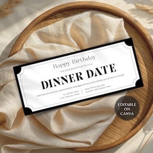 May include: A black and white dinner date gift voucher with the text "Happy Birthday" and "Dinner Date". The voucher is on a wooden tray with a beige cloth and dried plants.