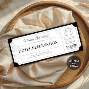 以下が含まれることがあります： 「Happy Birthday」と「Hotel Reservation」の文字が入った、白黒のホテル予約券。名前とパーソナライズされたメッセージを追加するスペースがあります。木製のトレイの上に、クリーム色の布が敷かれています。