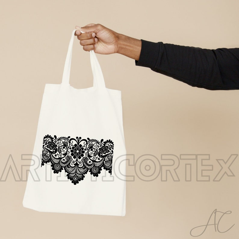 Peut inclure: Sac fourre-tout blanc avec un motif de dentelle noire. Le sac est tenu par une main.