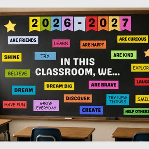 Könnte beinhalten: Eine große schwarze Klassenzimmertafel mit dem Text IN THIS CLASSROOM, WE..., umgeben von bunten rechteckigen Schildern mit Wörtern wie ARE FRIENDS, LEARN, ARE HAPPY, SHINE, TRY, ARE KIND, BELIEVE, DREAM, DREAM BIG, ARE BRAVE, EXPLORE, LAUGH, HAVE FUN, GROW EVERYDAY, DISCOVER, TRY NEW THINGS, SMILE, CREATE, HELP OTHERS und den Jahren 2026-2027.