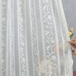 May include: White sheer curtain with a delicate floral lace pattern. The lace features a repeating design of small flowers and leaves.