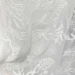 Puede incluir: Tela blanca transparente con un patrón floral bordado. La tela es delicada y tiene una textura suave y fluida.