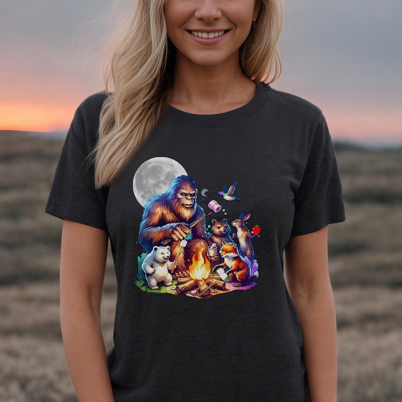 May include: A dark grey t-shirt with a graphic of Bigfoot roasting marshmallows around a campfire with a fox, rabbit, and two polar bears. The moon is in the background.