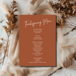 May include: A Thanksgiving menu card with a burnt orange background and elegant white script. The menu lists starters, main courses, side dishes, and desserts, including roasted turkey, apple pie, and cranberry sauce.