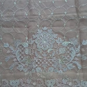 May include: White embroidered fabric with a floral design and a repeating pattern of circles. The fabric has a sheer, delicate texture and is embellished with small, iridescent sequins. The text "sleeve" is visible in the upper left corner of the image.