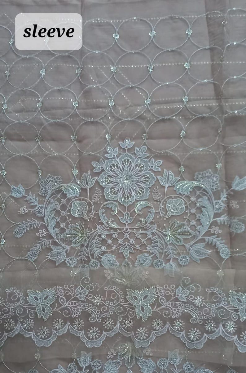 May include: White embroidered fabric with a floral design and a repeating pattern of circles. The fabric has a sheer, delicate texture and is embellished with small, iridescent sequins. The text "sleeve" is visible in the upper left corner of the image.