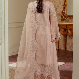 May include: A blush pink Pakistani shalwar kameez with intricate embroidery and lace detailing. The outfit features a long, flowing dupatta with a delicate floral pattern.