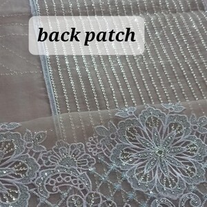 May include: A close-up of a sheer fabric with a silver glitter pattern. The fabric has a delicate lace trim with a floral design. The text "back patch" is visible in the image.