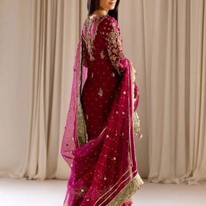 May include: A magenta embroidered dress with a matching sheer dupatta. The dress features gold and green embellishments and a deep V-neckline.