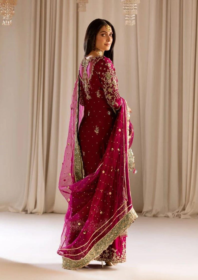 May include: A magenta embroidered dress with a matching sheer dupatta. The dress features gold and green embellishments and a deep V-neckline.