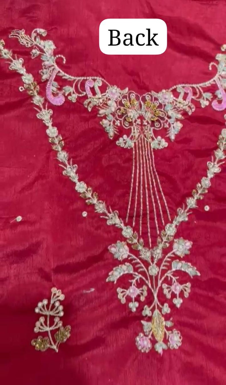 May include: A close-up of a red fabric with intricate embroidery in white, gold, and pink. The embroidery features floral designs and a central motif that resembles a stylised tree.