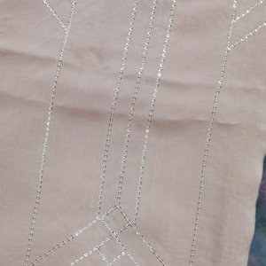 May include: A light brown trouser with a silver sequined design. The design features a geometric pattern with lines and angles.