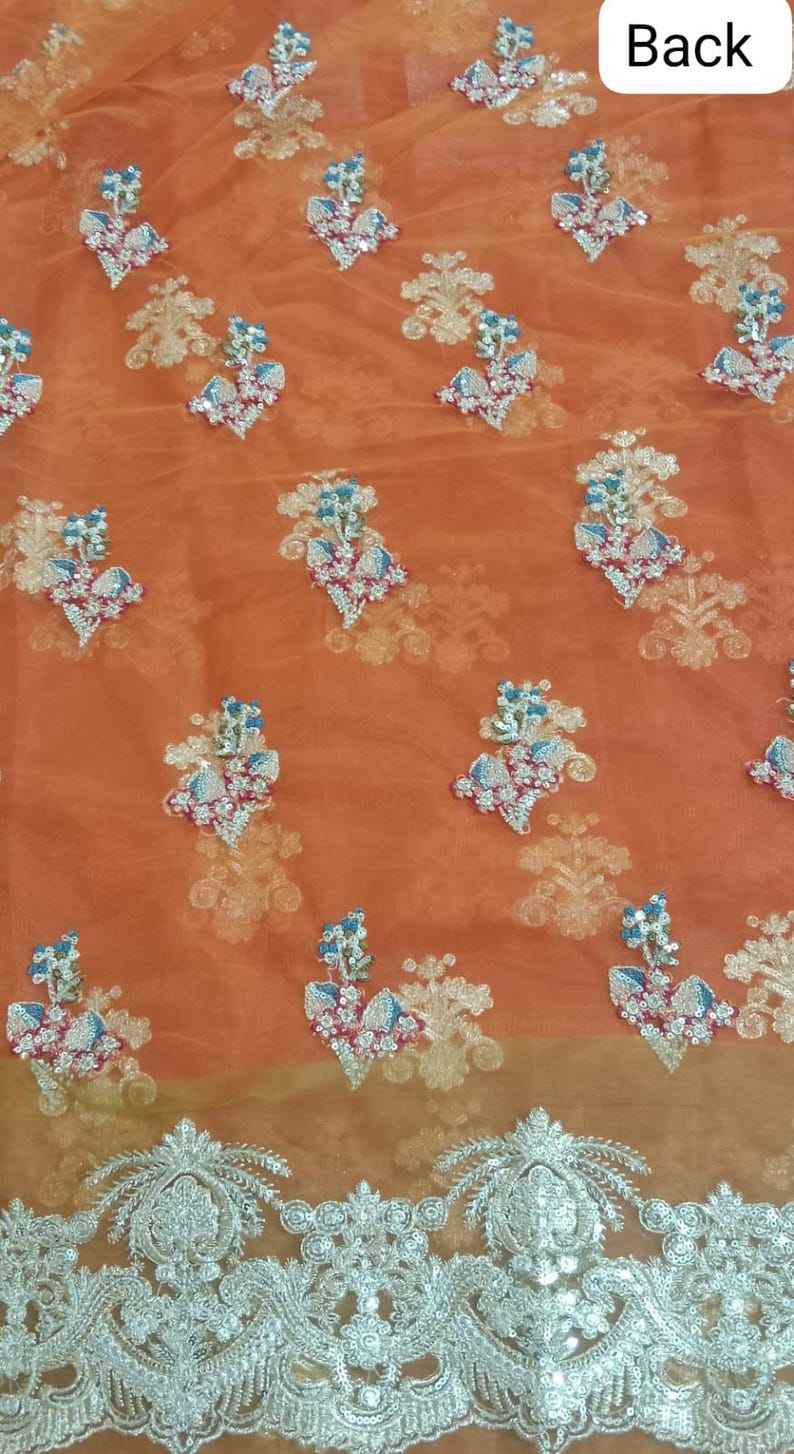 Op de afbeelding: Oranje doorzichtig stof met zilveren geborduurde bloemenmotieven. De stof heeft een delicate, kant-achtige rand.