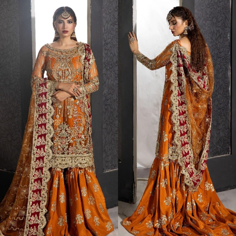 Op de afbeelding: Een vrouw draagt een traditionele Indiase outfit met een lange, oranje rok, een bijpassend topje en een doorschijnende, maroon dupatta met gouden borduurwerk. De outfit is versierd met ingewikkelde gouden en zilveren versieringen.