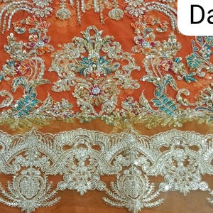 Op de afbeelding: Oranje stof met ingewikkelde zilveren en turquoise borduurwerk. De stof heeft een delicate kantversiering. Het woord "Daman" staat in witte tekst op de stof.