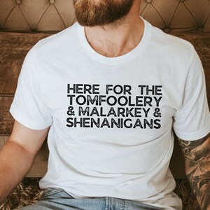 May include: White t-shirt with black text that reads "Here for the Tomfoolery & Malarkey & Shenanigans".