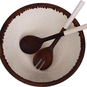 May include: A white ceramic salad bowl with a brown wooden rim and a brown wooden salad spoon and fork.