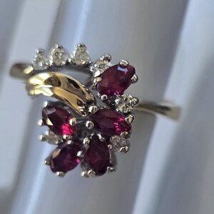 May include: A gold and silver ring with a cluster of marquise-cut ruby gemstones and small diamonds. The ring has a floral design, with the rubies at the centre and diamonds on the side.
