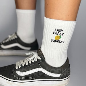 Könnte beinhalten: Weiß gerippte Socken mit dem Text "EASY PEASY SQUEEZY" und einer Zitronengrafik. Die Socken werden mit schwarz-weißen Turnschuhen getragen.