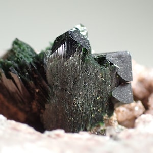 May include: A cluster of dark green, metallic, and lustrous crystals on a pink and white matrix. The crystals are sharp and well-defined.