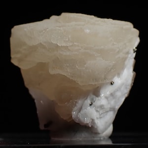 May include: A cluster of white and translucent calcite crystals with a layered, stacked appearance. The crystals have a slightly off-white color and are set against a black background.