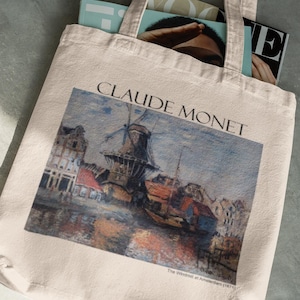 May include: A white canvas tote bag with a painting of a windmill by Claude Monet. The painting is titled "The Windmill at  Amsterdam 1871".