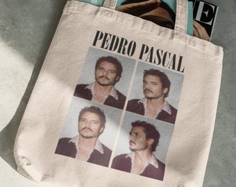 May include: A beige tote bag featuring a black and white image of Pedro Pascal. The image is a collage of four photographs of Pascal, each with a different expression. The text "PEDRO PASCAL" is printed in black above the image.