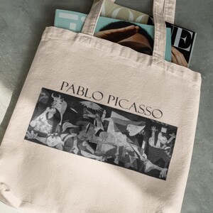 May include: A beige tote bag with the words "PABLO PICASSO" above a black and white image of a painting. The bag is filled with magazines. The bag has two handles.