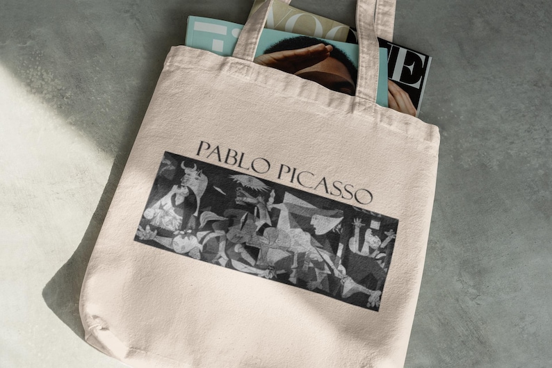 May include: A beige tote bag with the words "PABLO PICASSO" above a black and white image of a painting. The bag is filled with magazines. The bag has two handles.