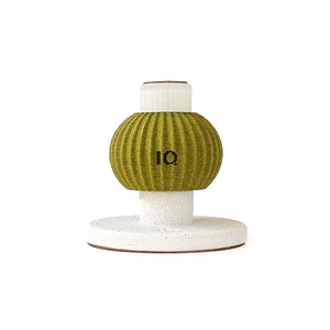 Peut inclure: Une lampe ronde verte texturée avec une base blanche et une étiquette noire "IQ". La lampe est sur une surface blanche.