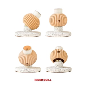 May include: Four beige ceramic candle holders with a ribbed texture and the letters "IQ" on the front. Each holder is on a white speckled base.