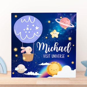 May include: A blue and purple hot air balloon with a white bunny inside, floating in a starry night sky. The text "Michael Visit Universe" is written below the balloon.