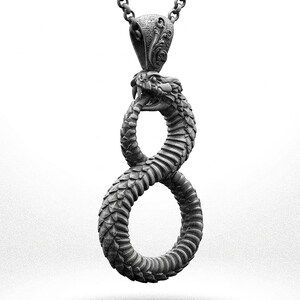 May include: A dark grey metal pendant shaped like a snake biting its own tail to form an infinity symbol. The snake features detailed scales and an open mouth with visible fangs. The pendant hangs from a matching dark grey metal chain link necklace.