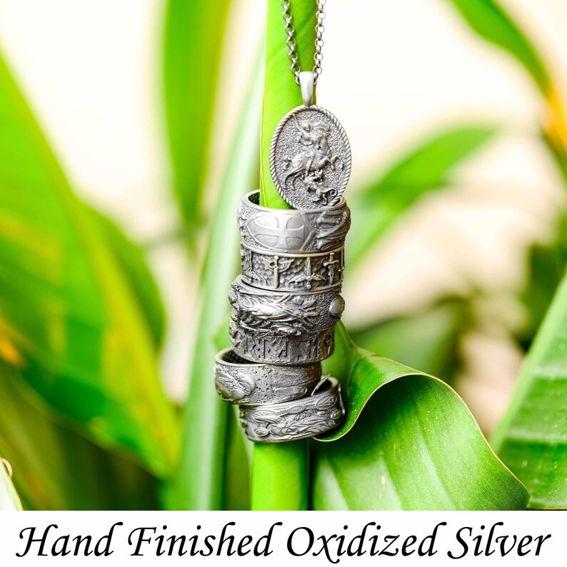 Puede incluir: Una pila de anillos de plata oxidada y acabada a mano y un collar con colgante. Los anillos est&aacute;n intrincadamente detallados con varios dise&ntilde;os. El colgante presenta un relieve detallado de una figura a caballo. El texto "Hand Finished Oxidized Silver" est&aacute; en la parte inferior.