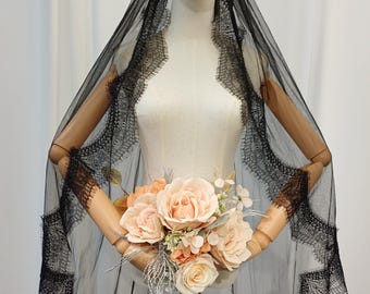 May include: A black lace veil with a scalloped edge is draped over a mannequin. The veil is sheer, allowing the mannequin's form to be partially visible. A bouquet of peach and cream-colored roses and other flowers is held in front.