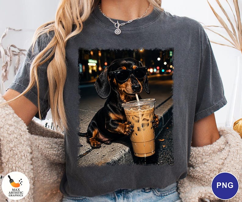 May include: A charcoal gray t-shirt featuring a graphic print of a black and tan dachshund wearing black sunglasses and holding a clear plastic cup filled with iced coffee, set against a blurred nighttime city street background.