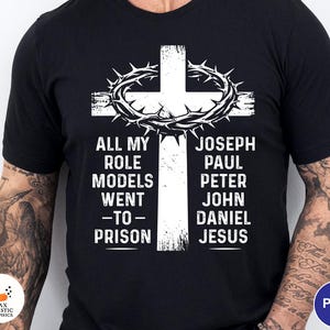 May include: Black t-shirt with a white cross design, a crown of thorns, and the text "ALL MY ROLE MODELS WENT -TO- PRISON". The names Joseph, Paul, Peter, John, Daniel, and Jesus are listed on the right side.
